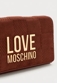 Brun ruskind pung med en tekstureret overflade, der har guld "LOVE MOSCHINO" tekst fremtrædende vist på forsiden.