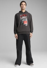 Felpa con cappuccio grigio scuro con una stampa grafica che presenta "Forza Milan" in lettere grasse. Abbinate a pantaloni neri e sneaker grigie.