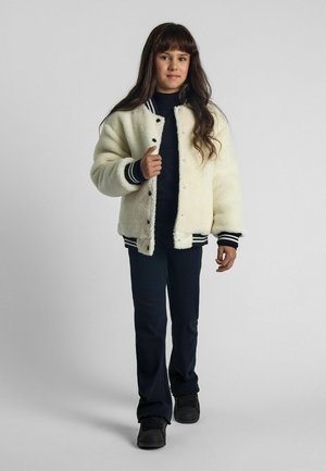 Witte neplederen bomberjack met zwarte drukknoopsluiting en gestreepte ribboorden, gecombineerd met een donkere broek en zwarte sneakers.