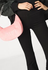 Pink faux suede handbag with "Juicy" in rhinestones. Rounded shape, chain strap, and textured surface displayed against black clothing.