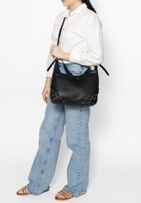 Zwarte leren handtas met een gestructureerd oppervlak, voorzien van dubbele handvatten bovenaan en zilveren hardware-accenten, gedragen op de schouder van een persoon.