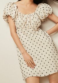 Vestido crema con mangas cortas abullonadas, con un patrón moteado en negro y escote gather. Tejido ligero con un ajuste relajado.