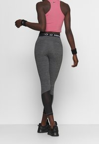 Leggings grigi alti in vita con dettagli in rete e design aderente, abbinati a un top sportivo corto rosa. Scarpe nere e un braccialetto visibili.