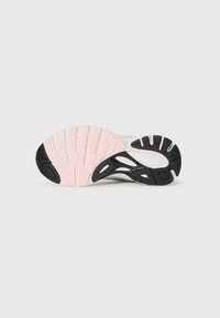 Semelle de chaussure de sport présentant un arrière en caoutchouc noir texturé, un intercalaire rose et un avant en blanc avec des canaux de flexion et des points de traction stratégiques.