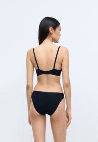 Fekete melltartó és hozzá illő bikini alsó, sima anyagból, állítható pántokkal és diszkrét logóval a derékpánton, hátulról bemutatva.