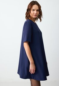 Abito blu navy a maniche corte con vestibilità ampia, colletto rotondo e tessuto liscio e strutturato. Linee pulite e orlo svasato.
