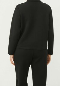 Veste noire ajustée à manches longues avec un col subtil, présentant une texture lisse et un design minimaliste, accompagnée d'un pantalon assorti.