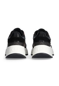 Para czarnych i brązowych sneakersów z grubymi białymi podeszwami, ukazanych od tyłu na białym tle.
