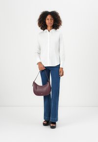 Camicia bianca con bottoni, jeans a zampa d'elefante blu e una borsa in pelle bordeaux. Sandali con zeppa e riccioli strutturati completano l'outfit.