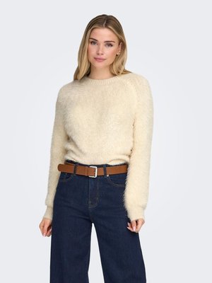 Maglione color crema soffice con maniche lunghe, scollo rotondo e polsini a coste, abbinato a jeans a gamba larga blu scuro e cintura marrone.