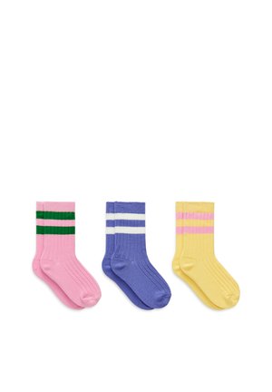 Trois paires de chaussettes côtelées rose avec des rayures vertes, bleu avec des rayures blanches et jaune avec des rayures roses, disposées côte à côte sur fond blanc.