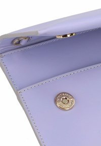 Fliederfarbene Lederbrieftasche mit glatter Textur, ausgestattet mit einem goldfarbenen Druckknopfverschluss und metallischem Branding im Inneren.