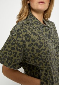 Grünes Hemdjackett mit Leopardenmuster und kurzen Ärmeln, aus Denim gefertigt, mit großen Knöpfen und Brusttaschen.