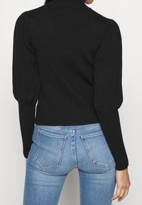 Zwarte geribbelde trui met pofmouwen en een cropped ontwerp. Gecombineerd met lichtblauwe highwaisted jeans met twee achterzakken.