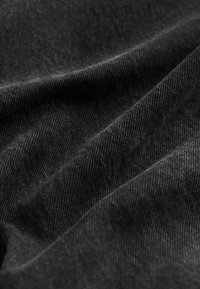 Schwarzer Denim-Stoff mit einer weichen Textur, der ein dezentes diagonales Webmuster aufweist. Die Oberfläche wirkt leicht abgenutzt und hat ein mattes Finish.