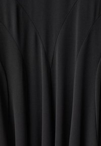 Schwarzes Kleid aus weichem, drapiertem Stoff mit strukturierten vertikalen Nähten und dezenten, geschwungenen Designlinien über der Brust.
