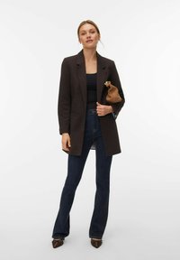 Smeđi sako s izrezanim reverima, nošen preko crne majice. Uparen s tamnoplavim trapericama s proširenim nogavicama i smeđim cipelama šiljastih vrhova, drži smeđi listić.