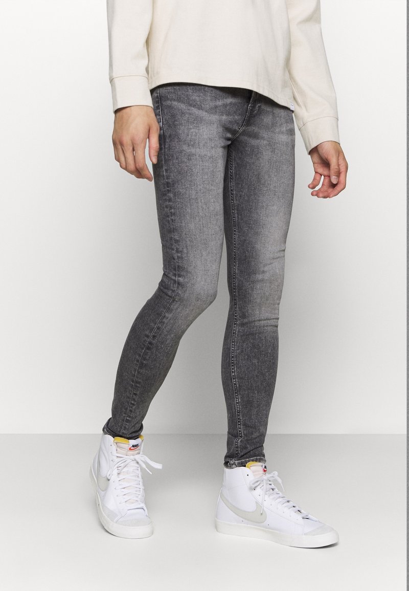 Jeans slim fit grises con un lavado desvanecido, que presentan una textura suave y un detallado de costuras, combinados con zapatillas altas blancas.