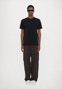 Tricou negru cu mâneci scurte, asortat cu pantaloni cargo maro, având multiple buzunare și o croială lejeră. Tenisi albi completează ținuta.
