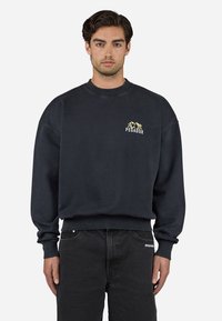 Mørkeblå sweatshirt med ribbet rund halsudskæring og manchetter, med et lille gult grafisk logo på brystet og loose fit design.