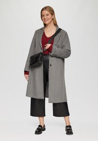 Grijze wollen blend jas, rode ribgebreide top, zwarte neplederen broek en zwarte instappers. Accessoires omvatten een kleine zwarte crossbody tas.