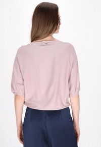 Top corto a maniche corte di un rosa chiaro e strutturato, con una vestibilità rilassata, caratterizzato da un design a cucitura curva sul retro e un piccolo etichetta vicino al collo.