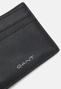 Black leather wallet with textured surface, featuring multiple card slots and silver branding. Neat stitching along the edges.