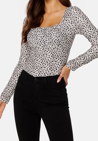 Långärmad topp i krämfärg med ett litet svart blommönster, med fyrkantig halsringning och en figurnära design, ihop med svarta jeans.