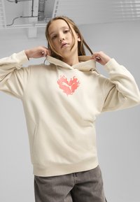 Sudadera beige con un bolsillo frontal, que presenta un logo de corazón en llamas rosa en el pecho. Textura suave, diseño casual con un corte holgado.