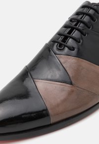 Scarpe da uomo in pelle nera e marrone con punta affusolata, caratterizzate da un design a colori misti, sezioni lisce e testurizzate, e chiusura con lacci.