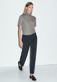 Grijze kortemouwen turtleneck top gecombineerd met donkerblauwe op maat gemaakte broek en bruine instappers. Glad materiaal met een strakke pasvorm en schone naden.
