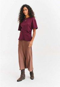 Bordowy top z krótkim rękawem z marszczonym detalem po bokach, zestawiony z brązową długą spódnicą i brązowymi zamszowymi botkami za kostkę z ozdobnymi klamrami.