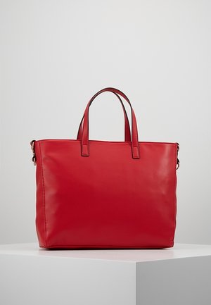 Czerwona torba na ramię ze skóry, z dwoma uchwytami, o prostokątnym kształcie i gładkiej fakturze, umieszczona na białym postumencie na tle jednolitego szarego tła.