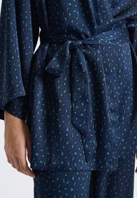 Indumento blu navy a motivi con macchie di leopardo verdi, dotato di una cintura in vita annodata e maniche ampie, realizzato in tessuto morbido.