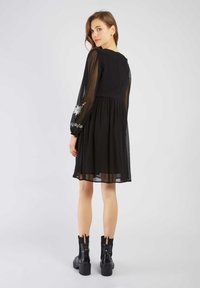 Zwarte jurk met doorzichtige lange mouwen met bloemmotieven; skaterstijl met een getailleerde top en een vloeiende rok; gecombineerd met chunky zwarte laarzen.