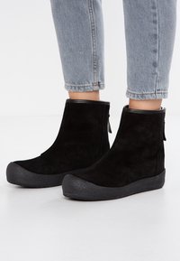 Bottines noires en daim avec une semelle en caoutchouc et un embout texturé. Présentent un haut lisse et une languette à l'arrière pour un enfilage facile.