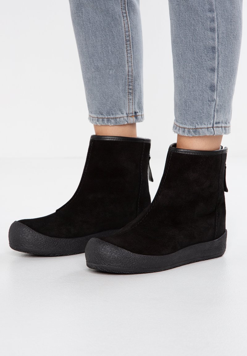 Bottines noires en daim avec une semelle en caoutchouc et un embout texturé. Présentent un haut lisse et une languette à l'arrière pour un enfilage facile.