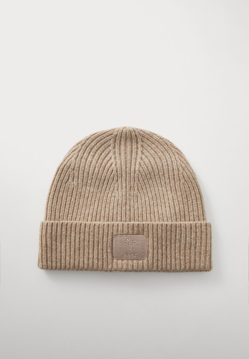 Gebreide beige beanie met geribbelde textuur, voorzien van een opvouwbare rand en een rechthoekig logo-patch in een contrasterende kleur aan de voorkant.