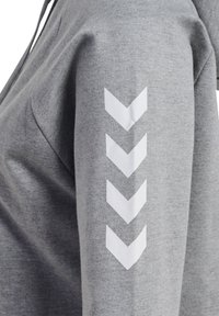 Sweatshirt cinza com um tecido texturizado, capuz e padrões de chevron brancos impressos na manga direita.