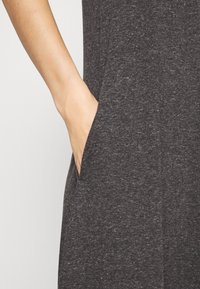 Tecido cinza escuro com um acabamento texturizado, apresentando um bolso lateral e uma vista em close de uma mão descansando perto da abertura do bolso.