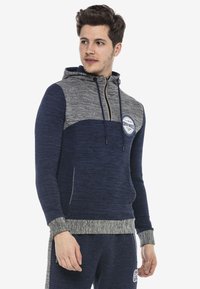 Navyblaue und graue Kapuzenjacke mit Reißverschluss, gerippten Bündchen und strukturiertem Finish. Verfügt über ein rundes Logo auf der Brust und seitliche Taschen.