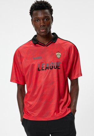 Rode voetbaltrui met een zwarte kraag, voorzien van grote zwarte tekst "LEAGUE" en "WINNER," met een logo erboven aan de linkerkant. Zachte textuur.