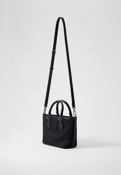 Kicsi fekete kézitáska, két rövid füllel és egy hosszú, állítható vállpánttal, egy sima világos háttér előtt bemutatva.