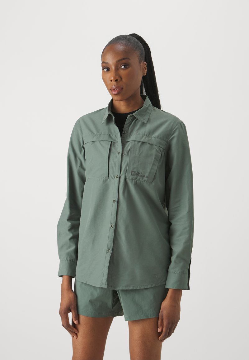 Camicia a maniche lunghe verde chiaro con due tasche sul petto, chiusura a bottoni e materiale morbido, abbinata a pantaloni corto coordinati.