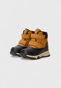 Botas impermeables marrones y negras con cuello acolchado, correas de velcro, suela de goma texturizada y detalle del logo en el lateral.