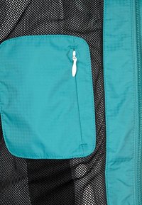 Tyrkysová látková kapsa se zipem na strukturovaném černém síťovém pozadí. Kapsa má zaoblené okraje a pevné švy.