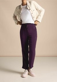 Lila lätta joggerbyxor med elastisk dragsko i midjan. I kombination med en vit t-shirt och en ljusbeige jeansjacka. Rosa och vita sneakers.