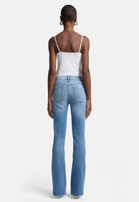 Jean évasé bleu clair avec un design classique à cinq poches et des détails cousus. Le tissu a une texture douce avec une finition lisse.