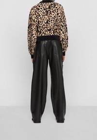 Pull en tricot à motif léopard avec un ourlet côtelé bleu marine, associé à un pantalon large en cuir noir taille haute avec poches arrière.