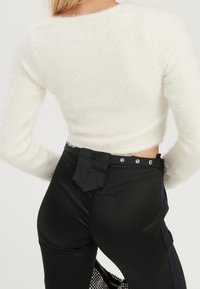 Tyst vit kort tröja i frotté möter högmidjade svarta byxor med en glänsande yta, och har sidopaneler samt knappdetaljer.